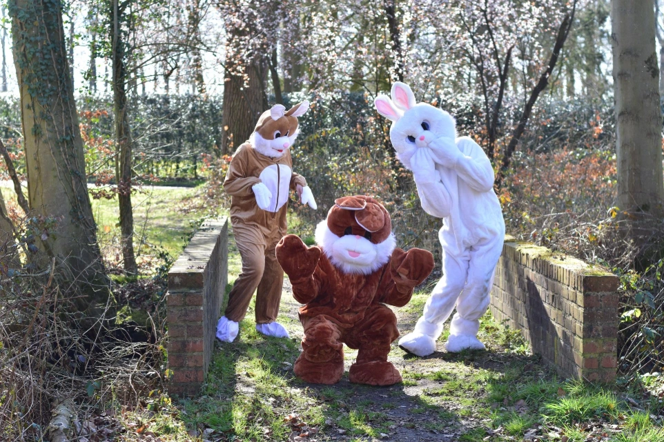 Groepsfoto buiten: Verschillende mensen en figuren (waaronder een paashaas) poseren samen in een tuin.