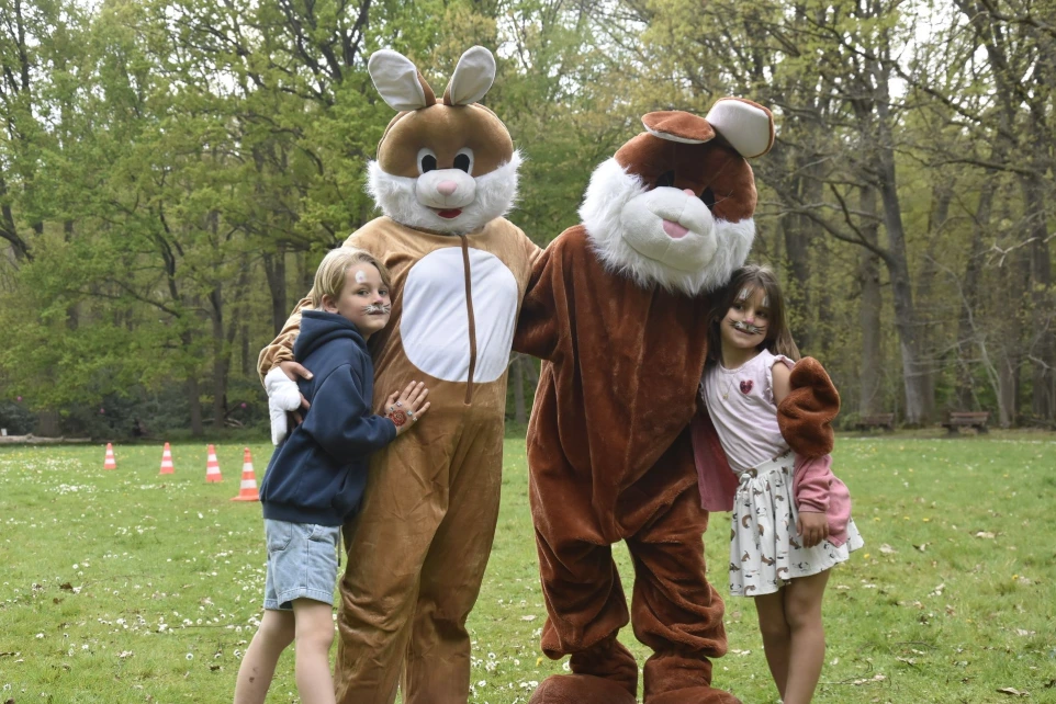 Twee mascottes: Een bruine en een witte haas staan samen buiten met een klein kind.
