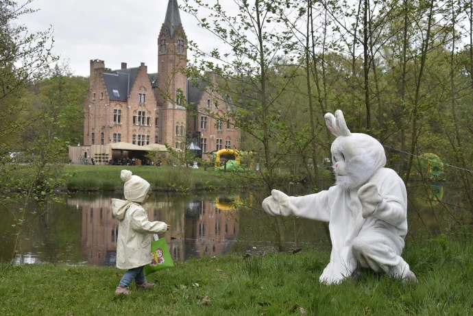 Paashaas in de tuin: Een witte paashaas staat buiten in een groene omgeving bij een stenen gebouw.