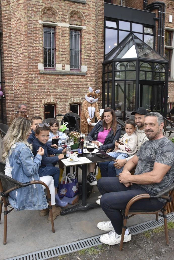 Gezelschap op terras: Een groep mensen zit buiten aan tafeltjes bij een historisch gebouw.