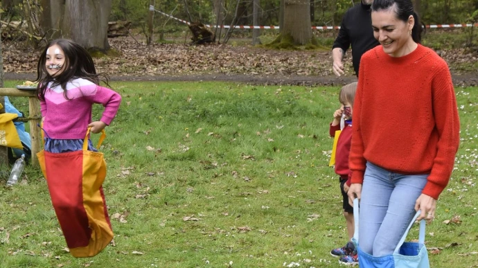 Kind op grasveld: Een kind loopt op een groen gazon met bomen op de achtergrond.